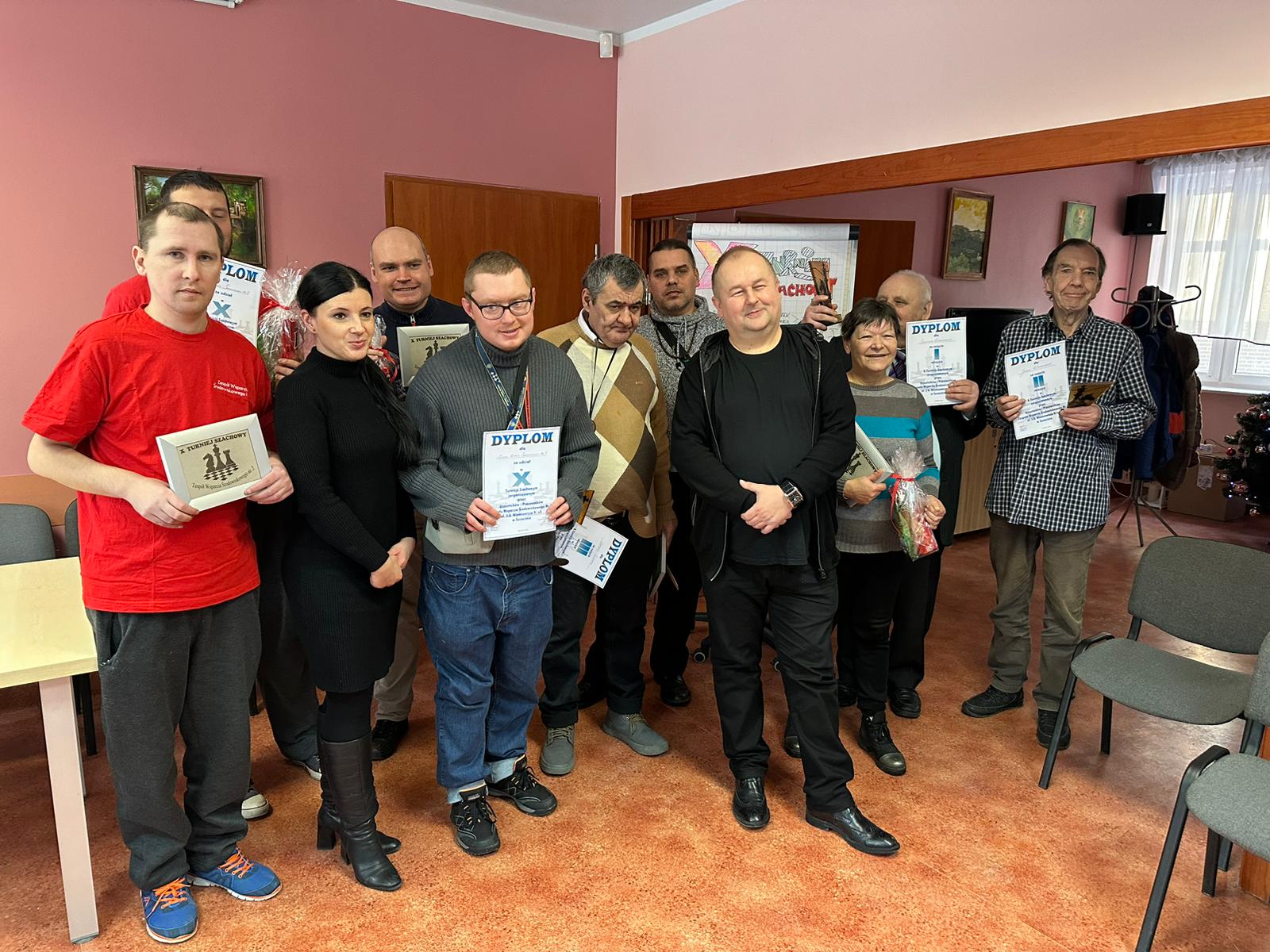 Grupa osób stoi z dyplomami z konkursu szachów.