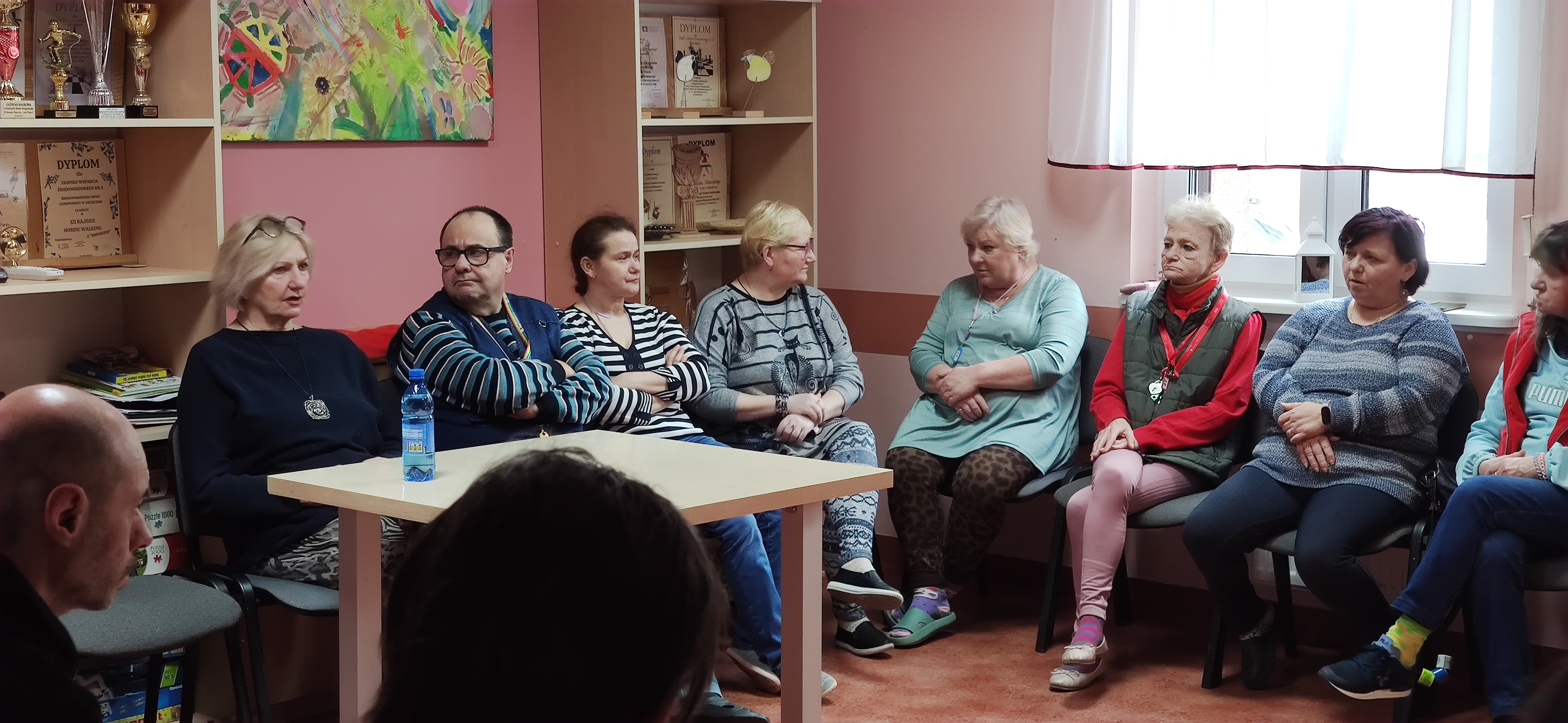 Grupa osób siedzi i słucha wykładu pielęgniarki środowiskowej.