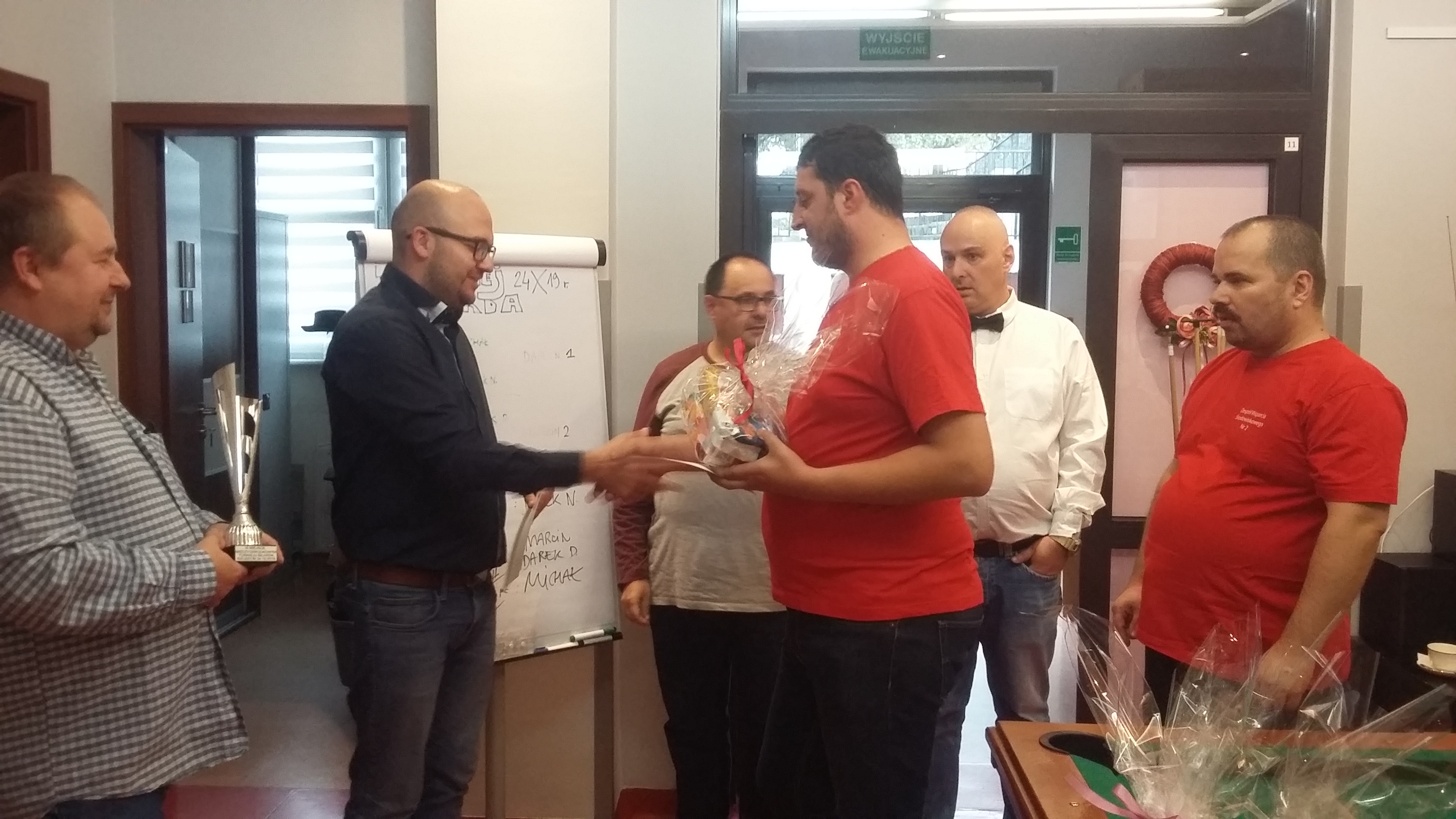 Sześciu mężczyzn stoi jeden trzyma puchar ,drugi podaje dłoń trzeciemu.