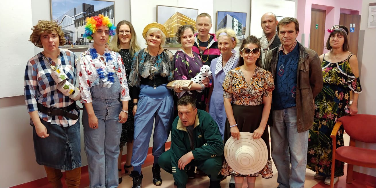 Grupa kobiet i mężczyzn w różnych przebraniach stoi na korytarzu