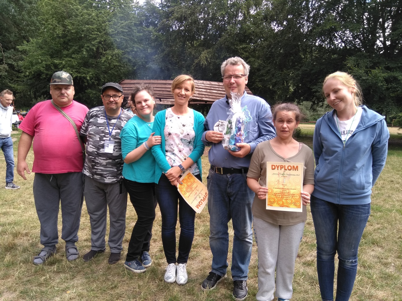 Cztery kobiety i trzech mężczyzn stoi i trzyma dyplomy na łące.