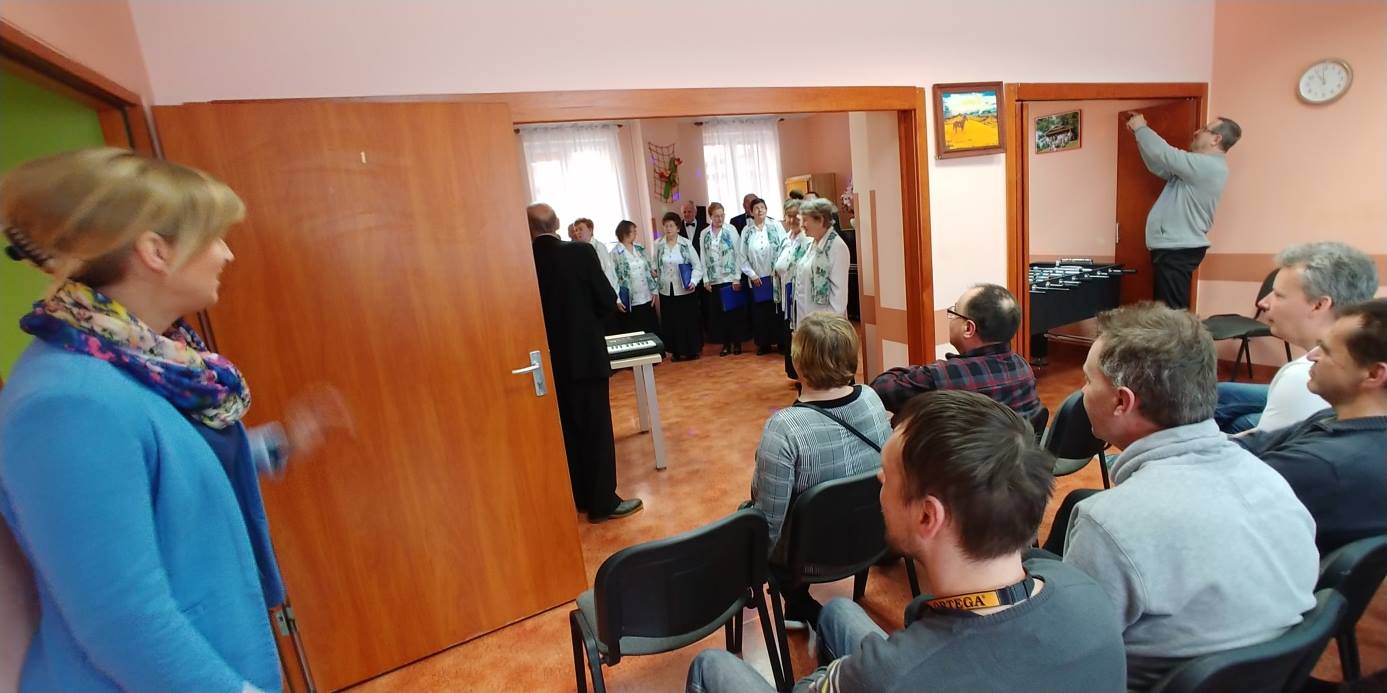 Chór starszych mężczyzn i kobiet .Jedna   kobieta stojąca na przeciw chóru.
