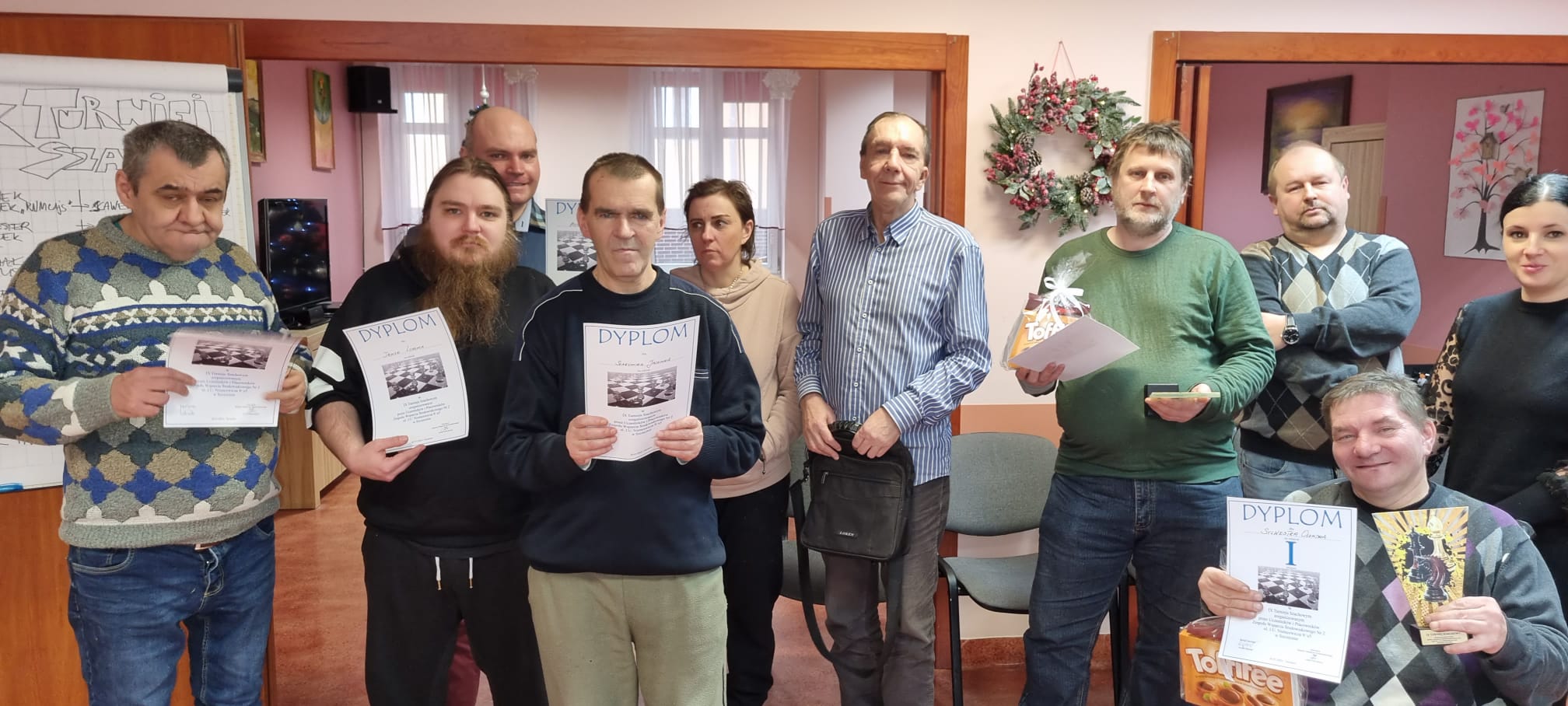 Grupa osób sto i z dyplomami za zajęte miejsca w zawodach szachowych.