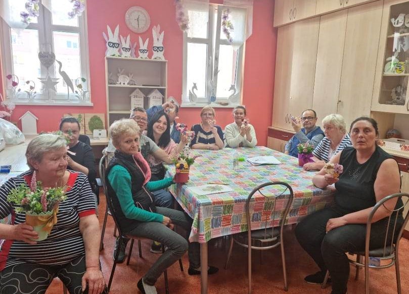 Grupa osób przy stole z prezentami na dzień matki.