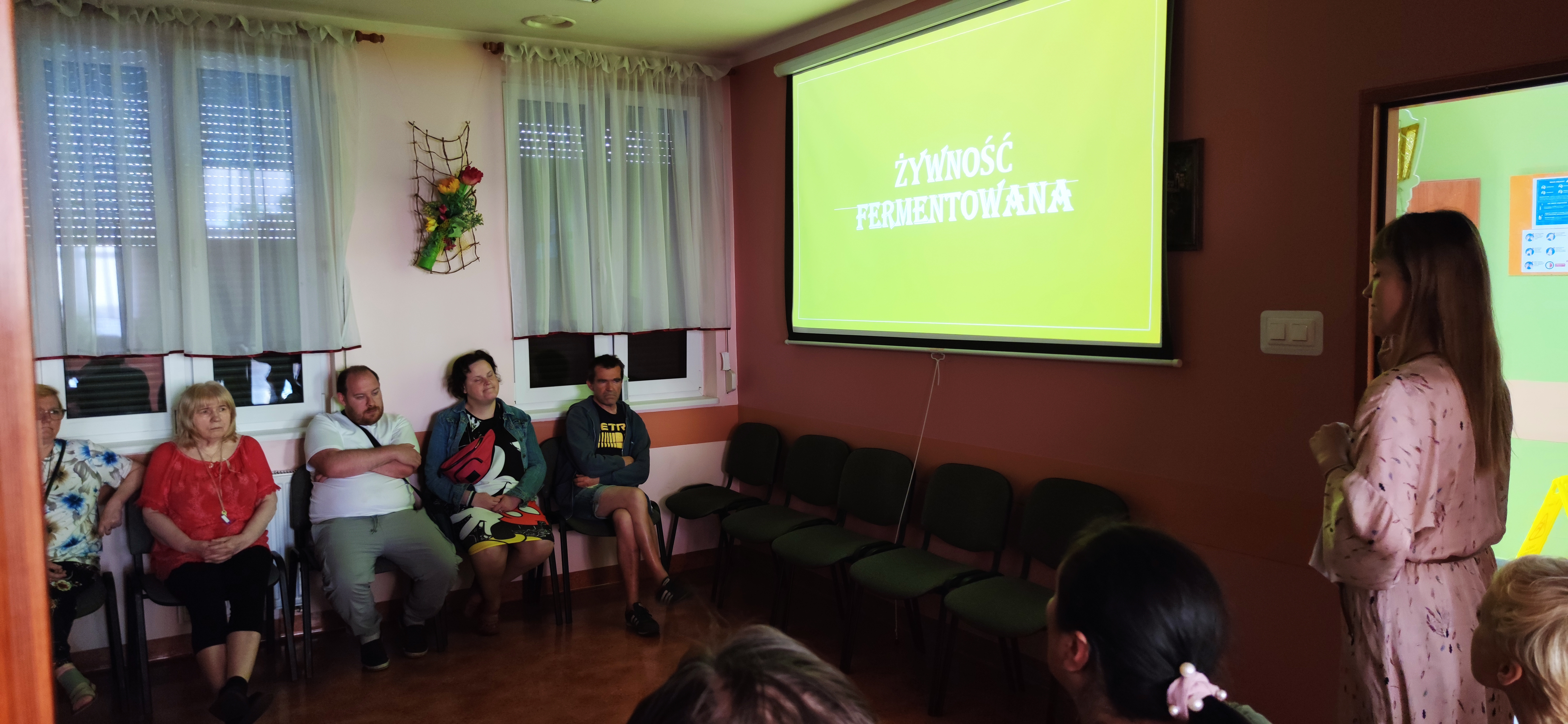 Grupa osób siedzi i słucha prelegentki.