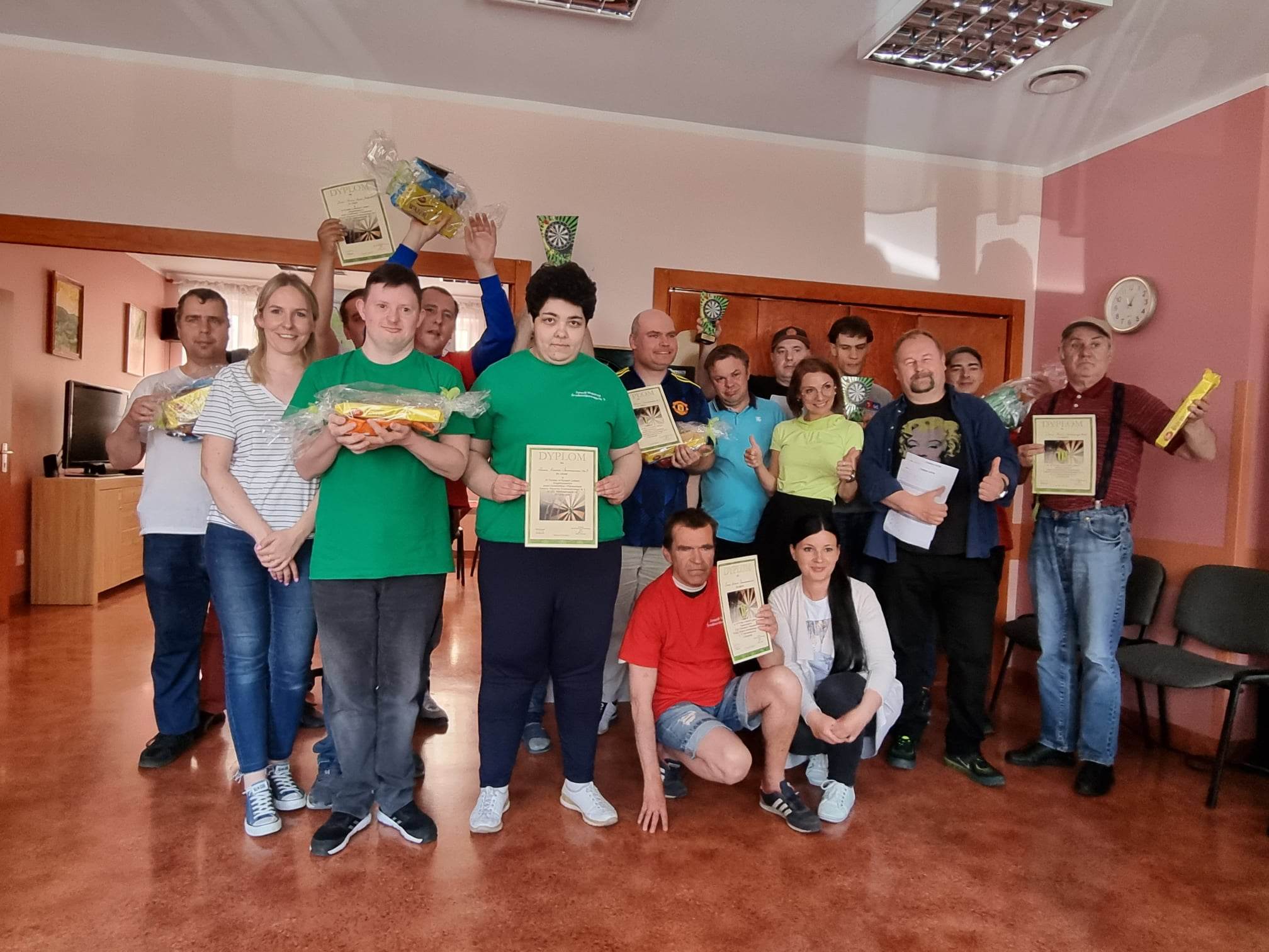 Grupa osób stoi z dyplomami pod tarczą do darta.