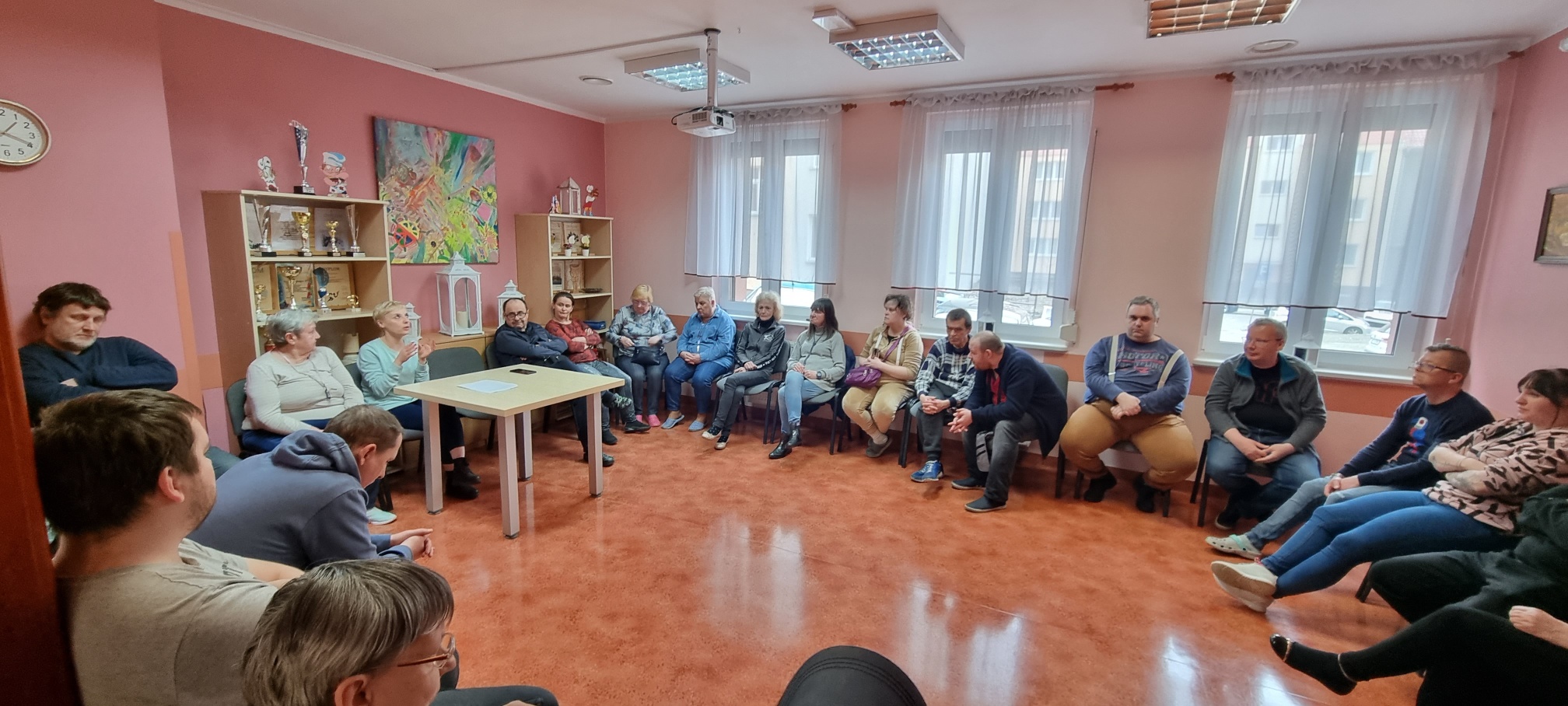 Grupa osób siedzi w kręgu i słucha pleregentki.
