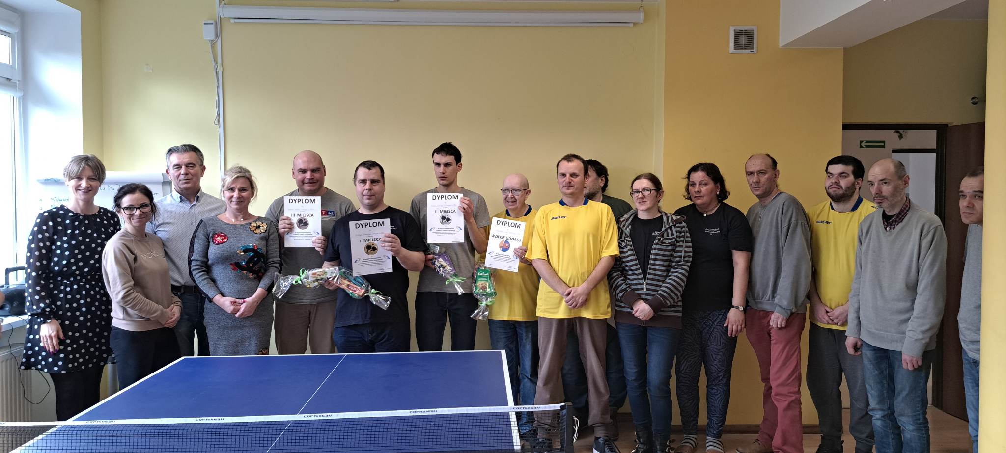 Grupa osób stoi za stołem do ping ponga z dyplomami.