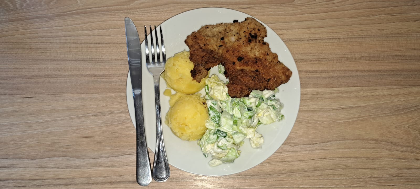 kotlet schabowy na talerzu z ziemniakami i surówką.