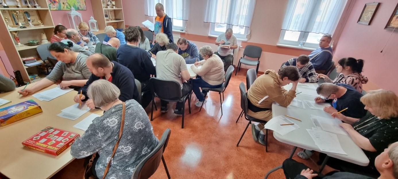 Grupa osób przy stołach rozwiązuje testy.