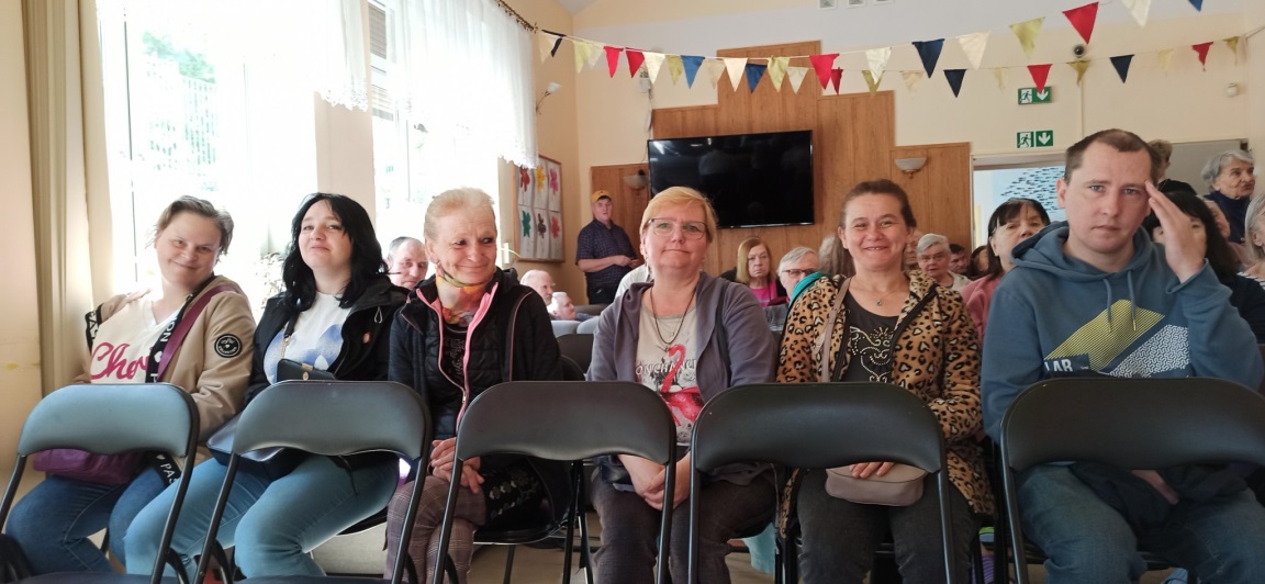 Grupa osób siedzi w pierwszym rzędzie na imprezie w DPS.