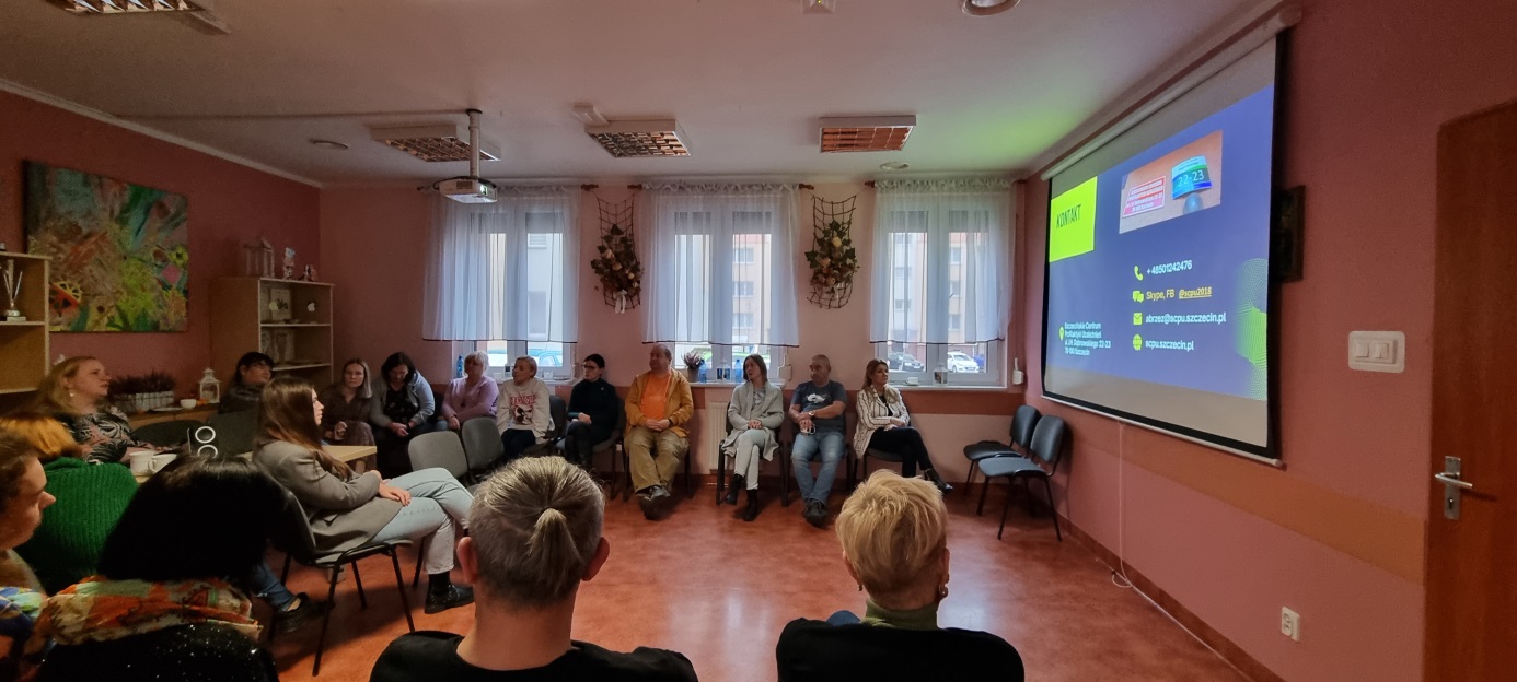 Grupa osób siedzi przed prelegentem który do nich mówi.