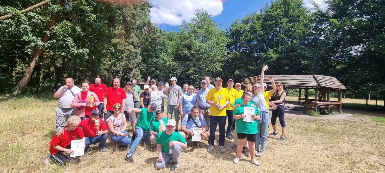 Grupa osób w strojach sportowych pozuje do zdjęcia grupowego na polanie w lesie.