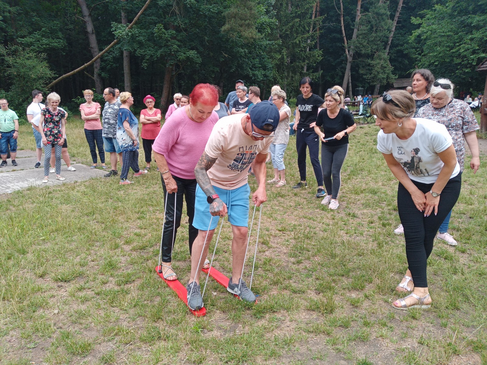 Ludzie stoją na zawodach na polanie leśnej.