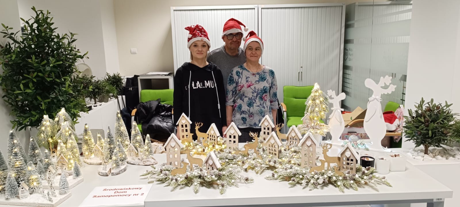 Dwie kobiety i mężczyzna stoją przed swoimi wyrobami na kiermaszu ozdób świątecznych.