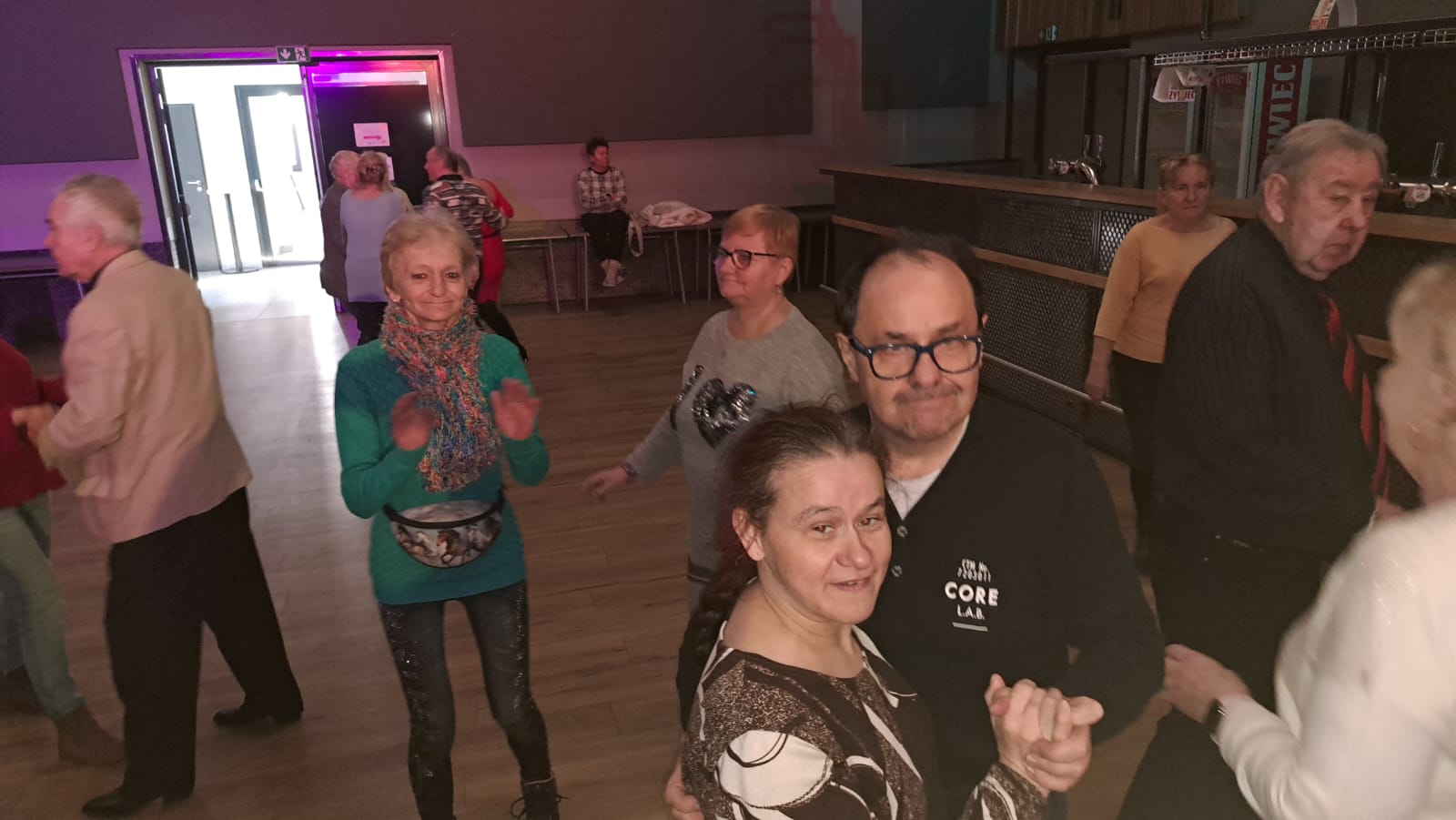 Grupa osób tańczy na widowni domu kultury.