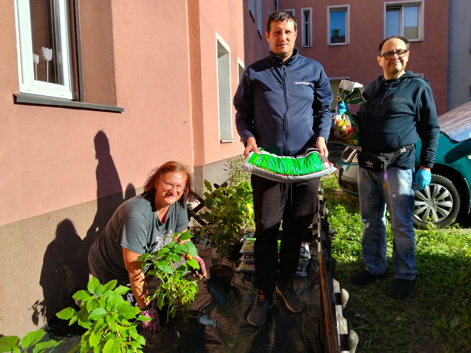 Trzy osoby pracują w ogródku przed ośrodkiem.