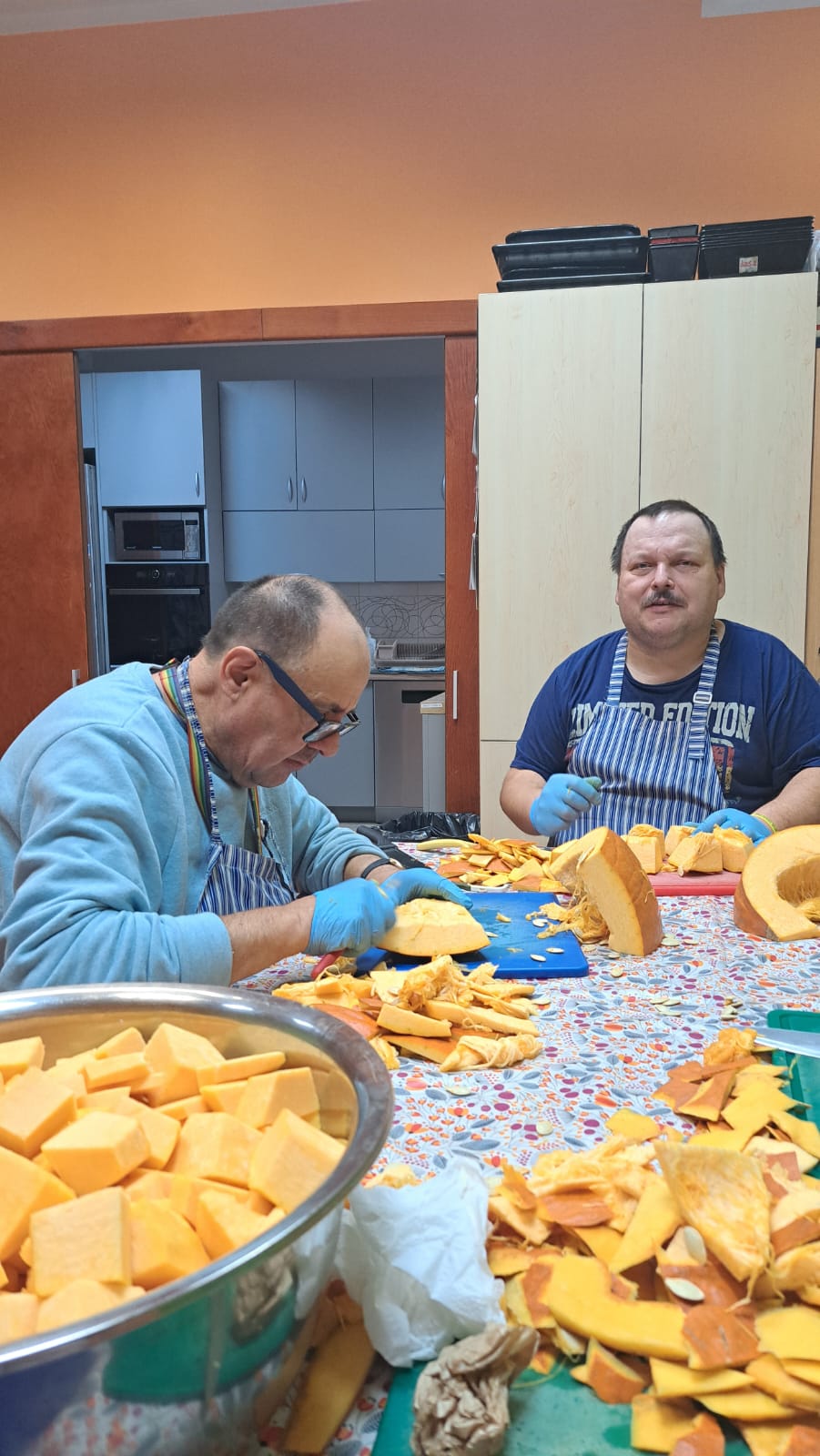 Dwie osoby z wielką dynią i jej już pokrojonymi kawałkami w kuchni.