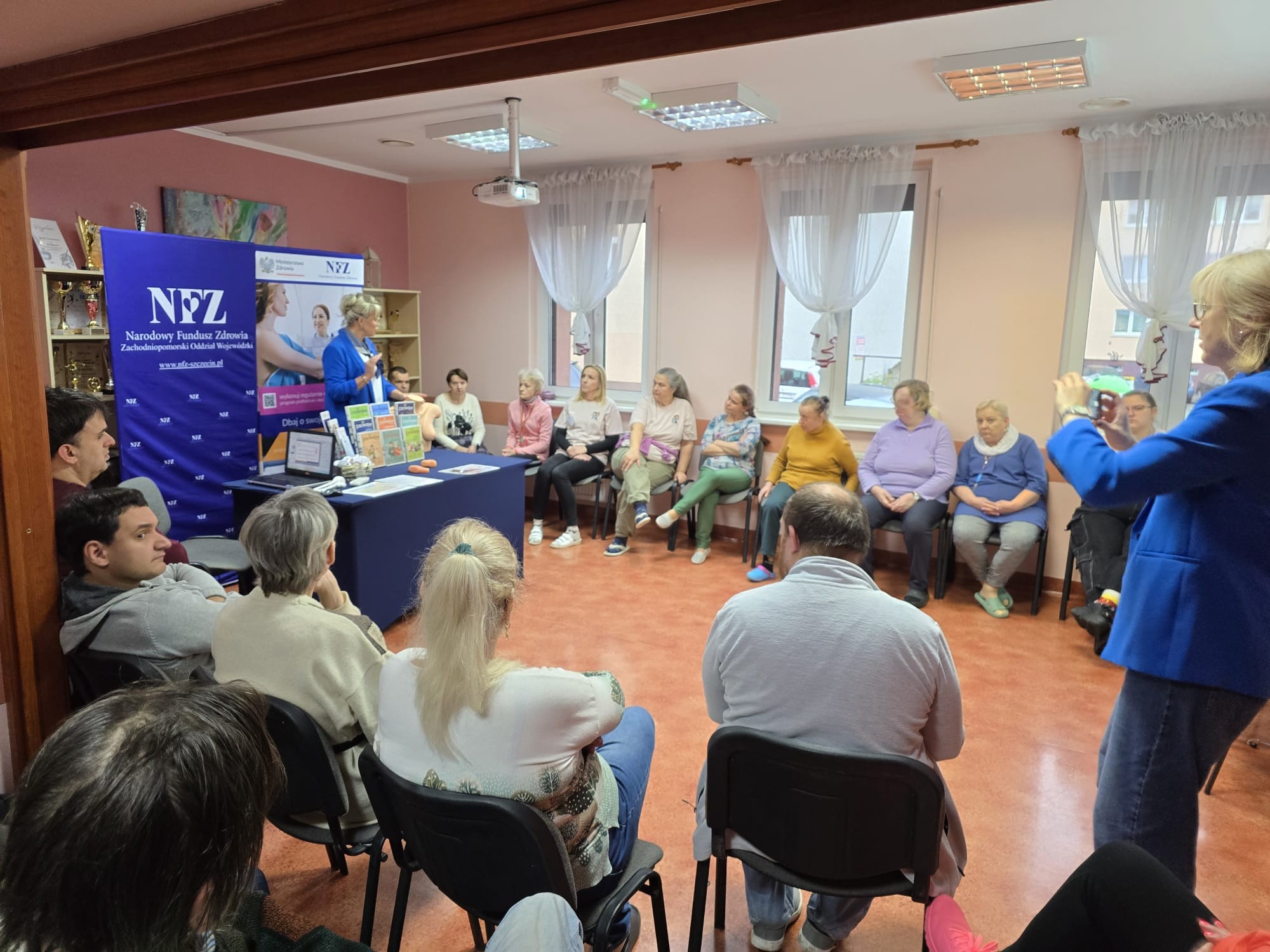 Grupa osób siedzi kręgu a prelegentka robi zdjęcie na pamiątkę.