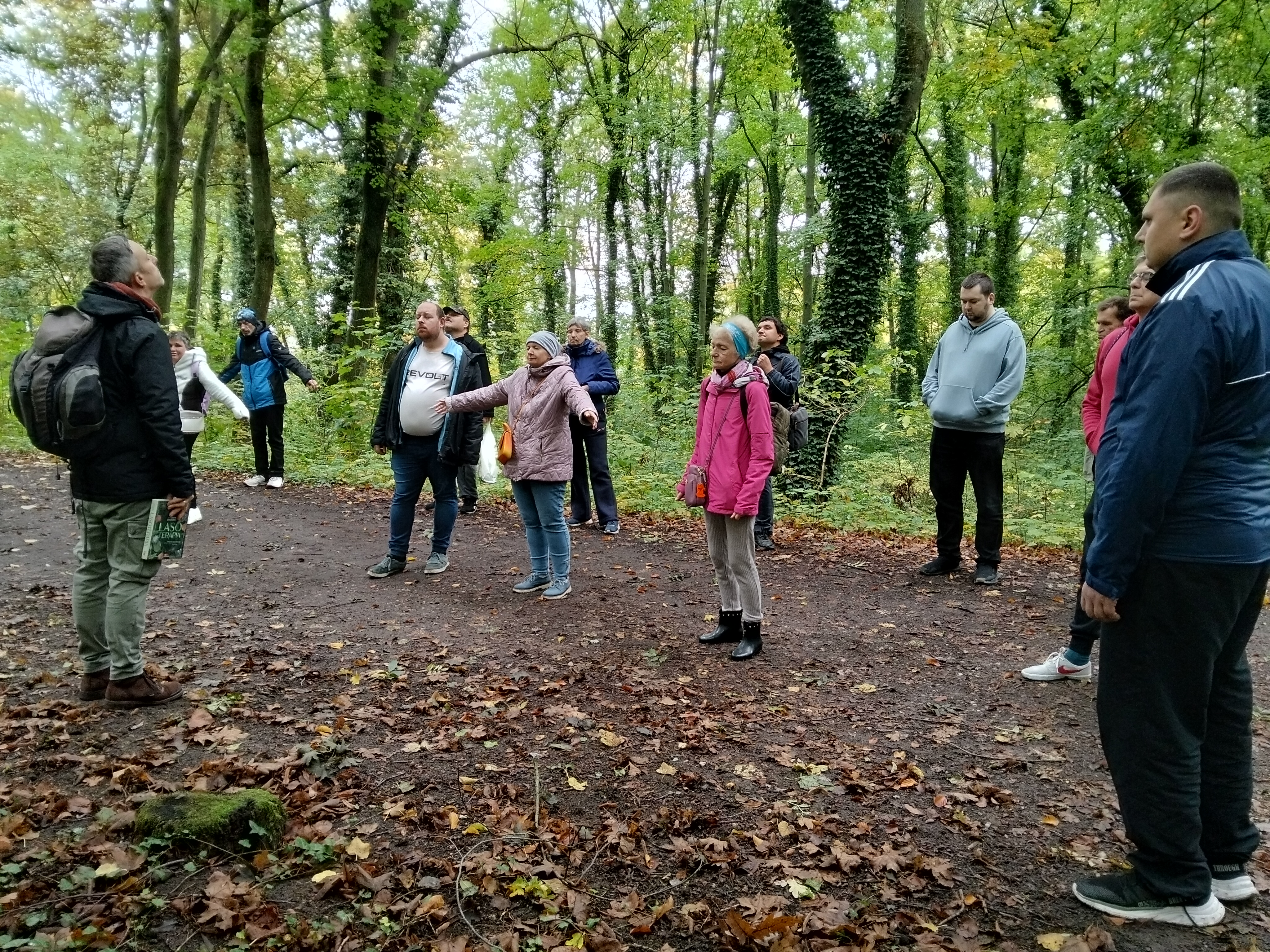 Grupa osób słucha wykładowcy w lesie.