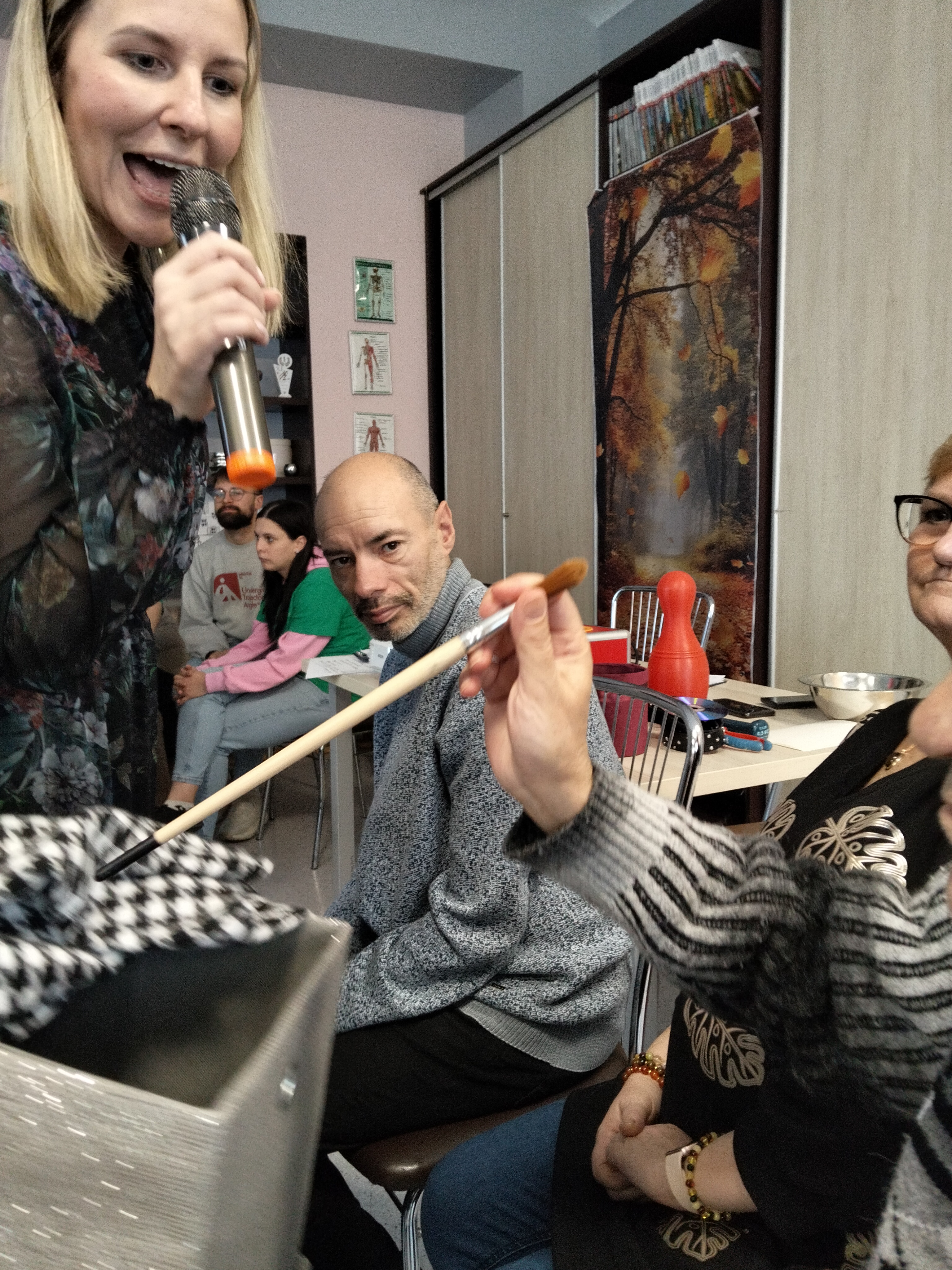 Dwie osoby na pierwszym tle ,jedna z mikrofonem,zabawa w zgaduj co jest w pudełku.