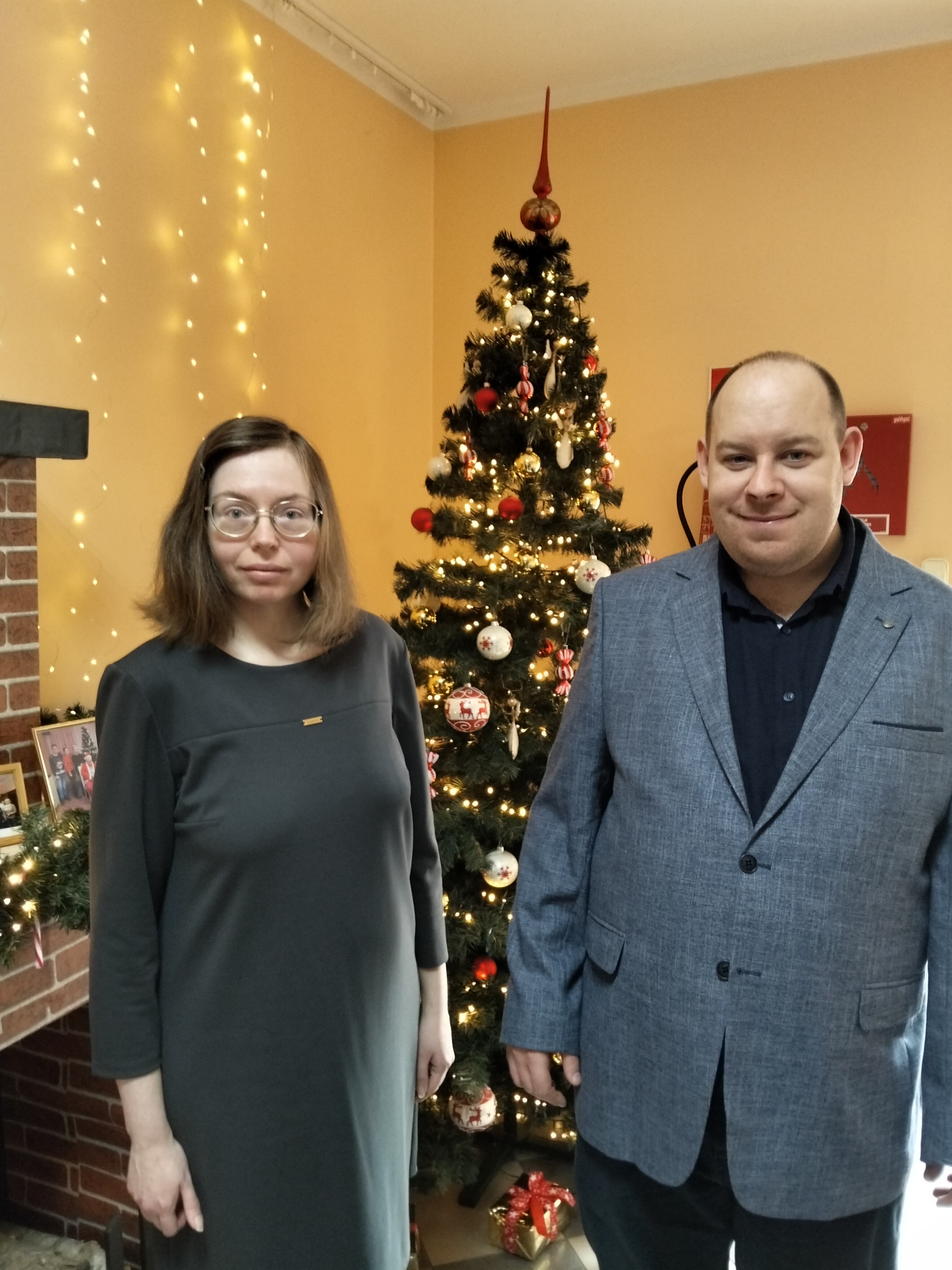 Dwie osoby ,kobieta i mężczyzna pozują na tle choinki.