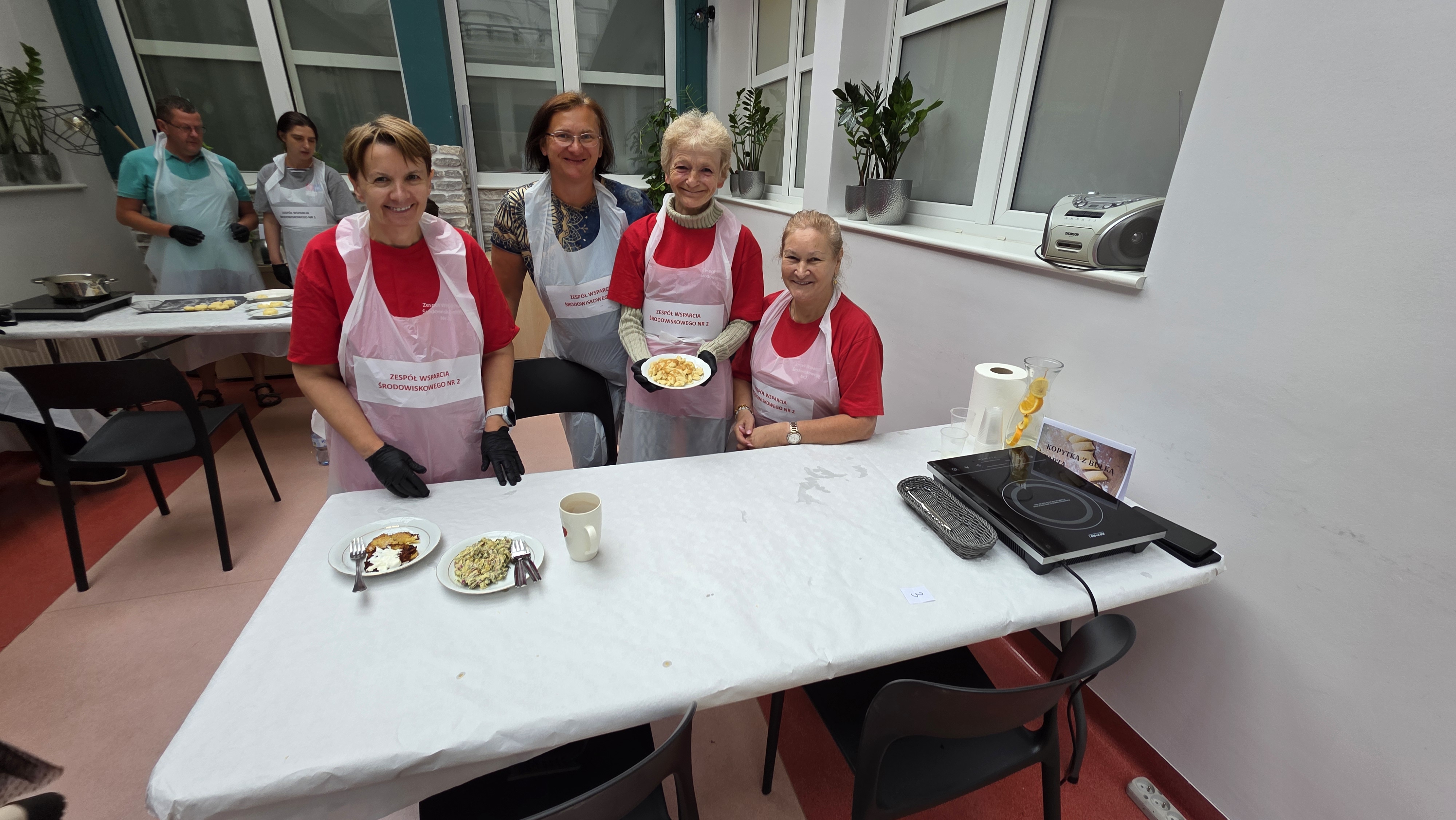 Grupa pań w fartuszkach z potrawą na talerzu wpatruje się w obiektyw.