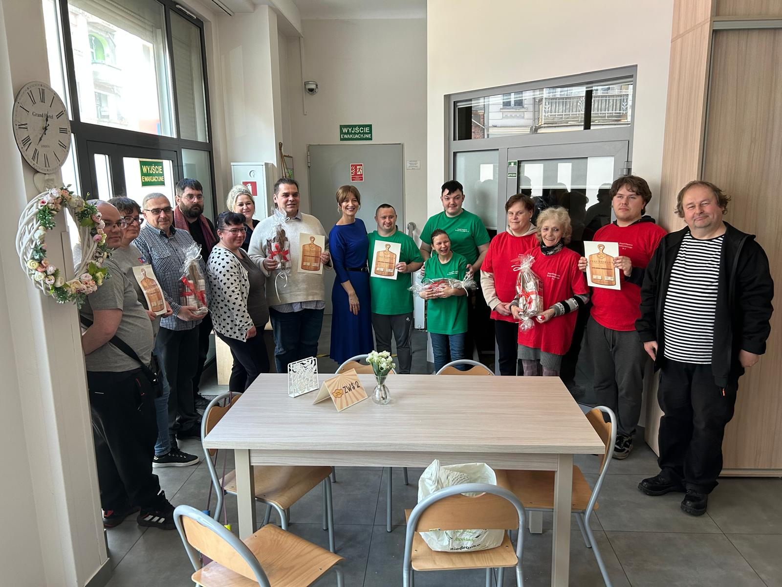 Duża grupa osób stojących w jednym rzędzie pozuje do zdjęcia; część z nich trzyma dyplomy i upominki.  