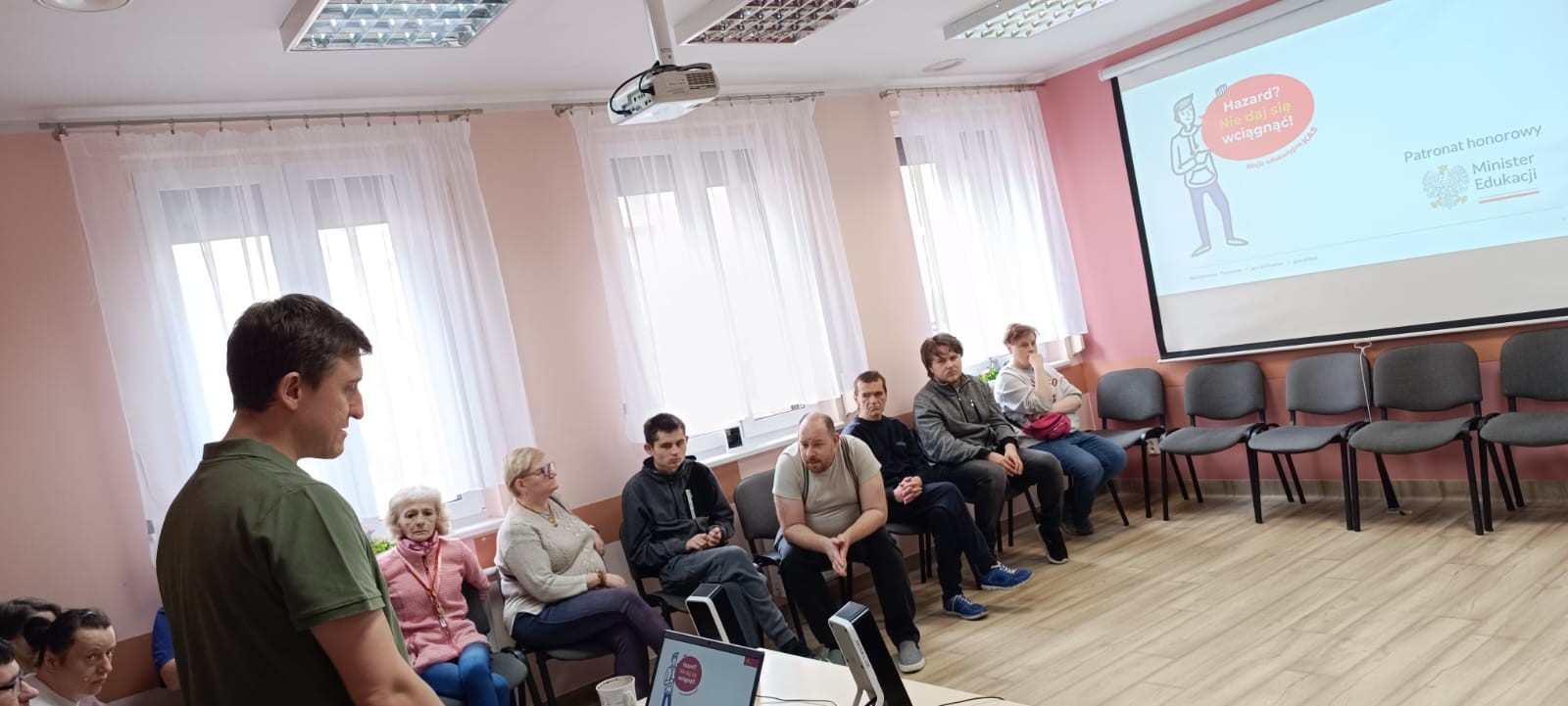 Mężczyzna prezentuje słuchaczom slajd z informacją o hazardzie.