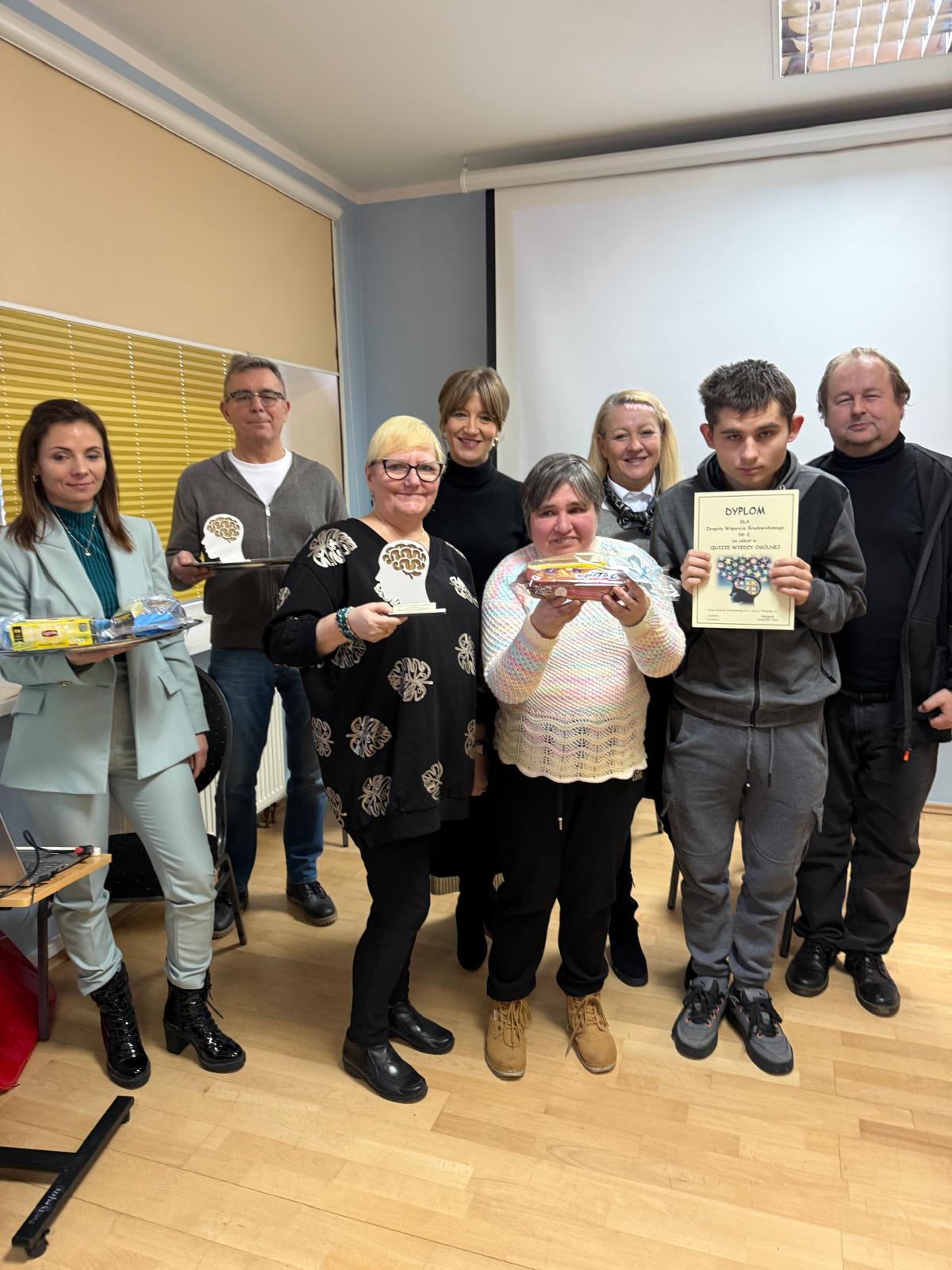 Grupa osób z dyplomami i nagrodą pozuje do zdjęcia.