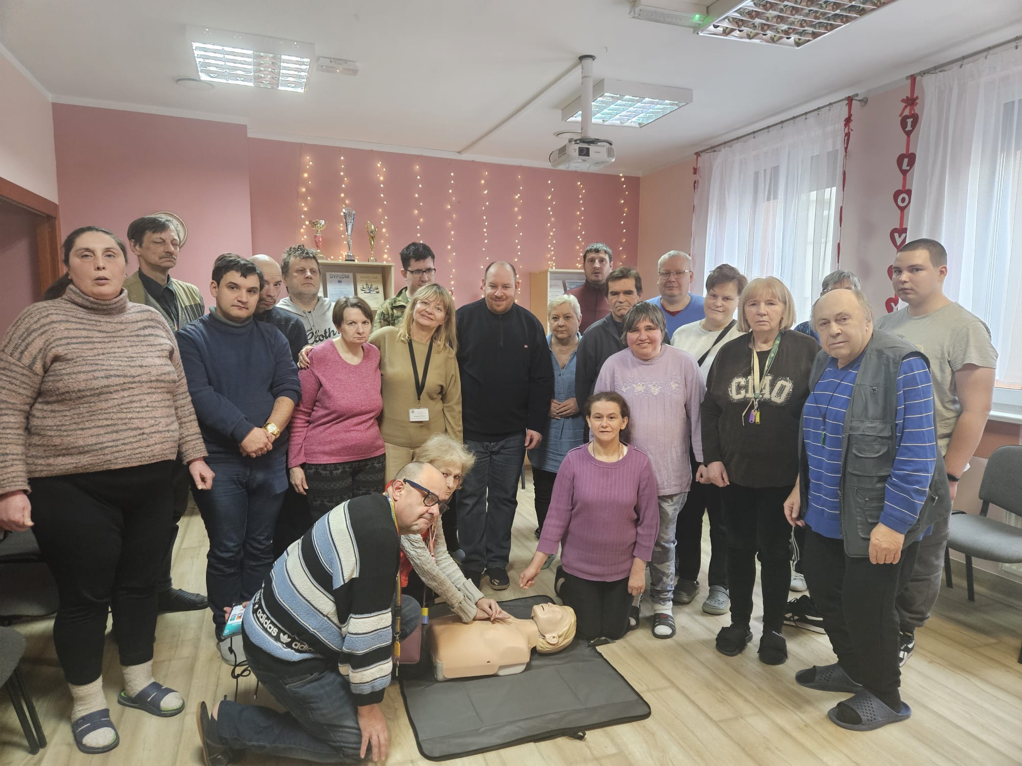 Grupa osób pozuje do zdjęcia stojąc a na materacu leży fantom do ćwiczeń dwie osoby klęczą.