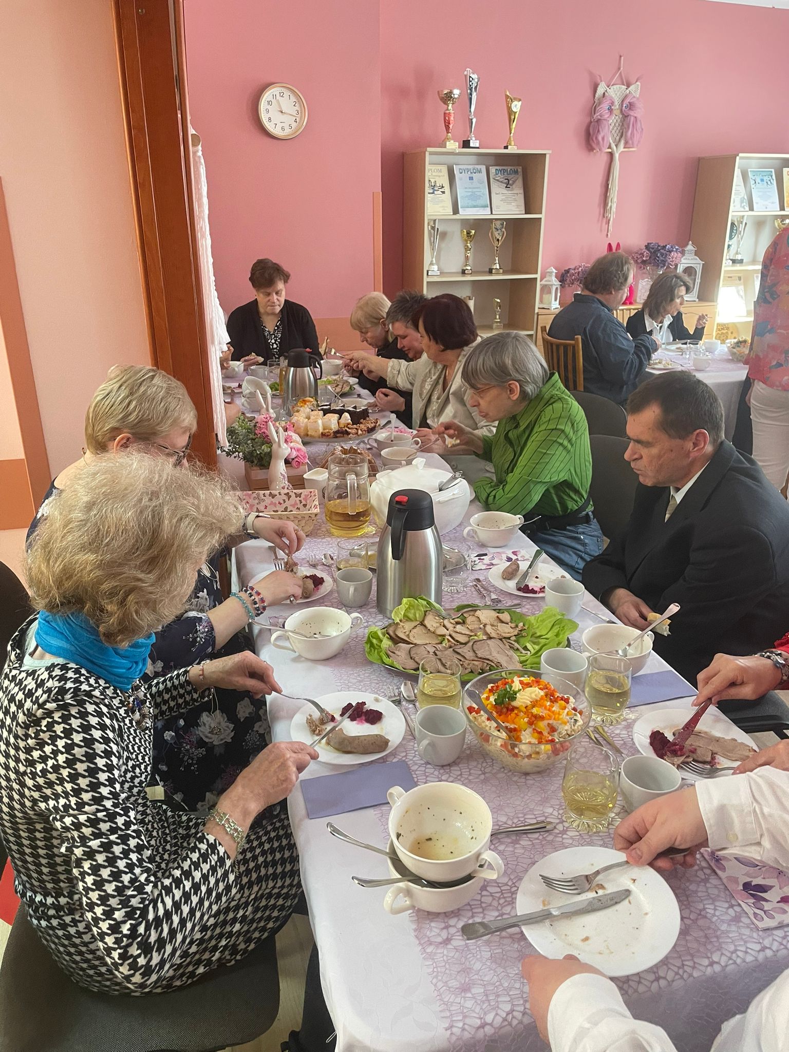 Grupa osób je śniadanie wielkanocne przy stole i  przy dekoracji wiosennej.  