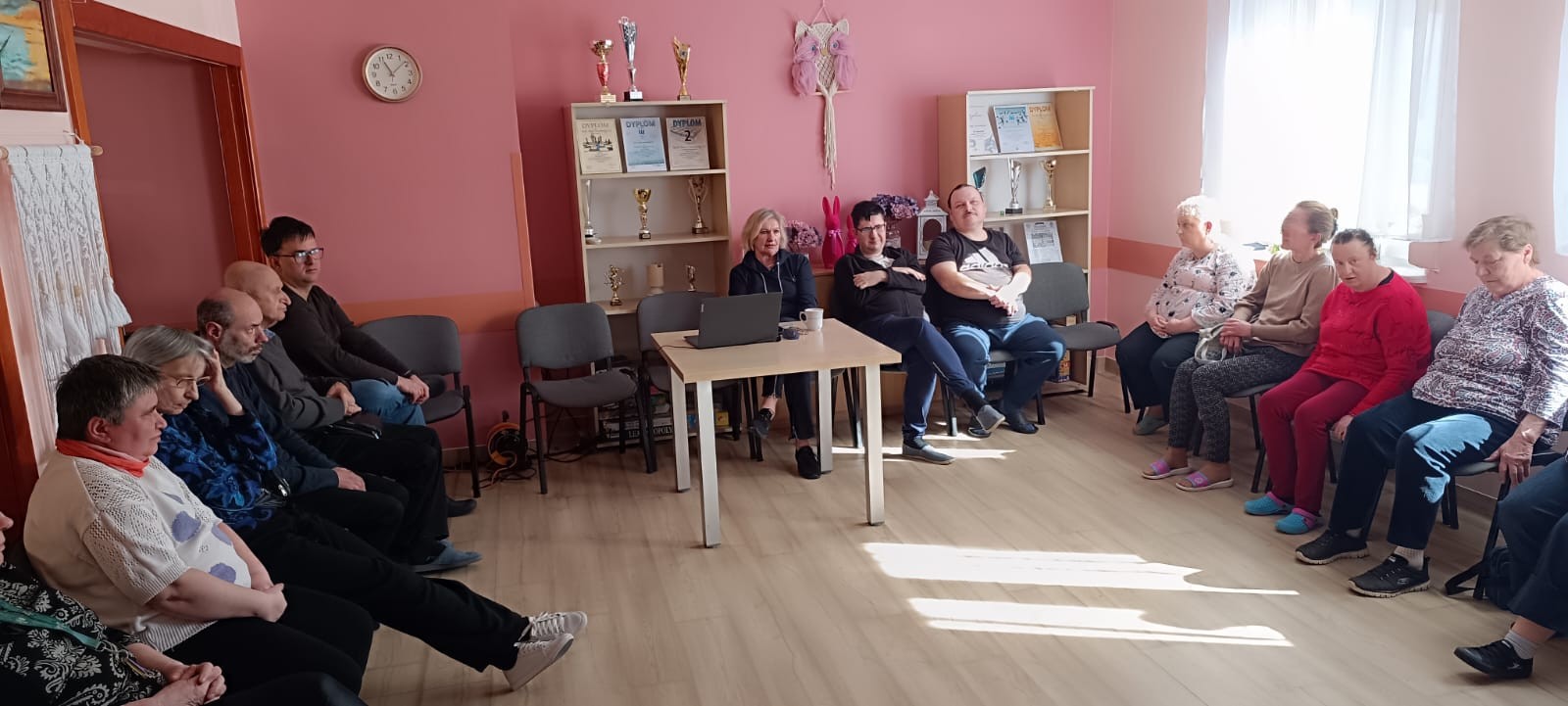 Grupa osób siedzi i słucha prelekcji pielęgniarki środowiskowej.