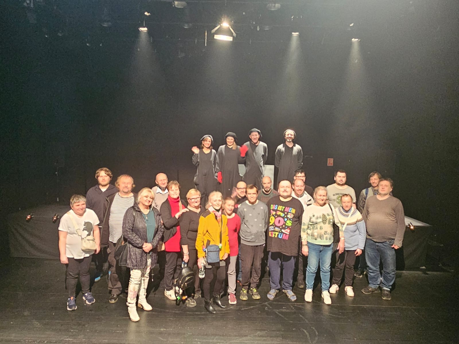 Grupa osób pozuje do zdjęcia z aktorami ubranymi w czarne kostiumy na scenie teatru Pleciuga
