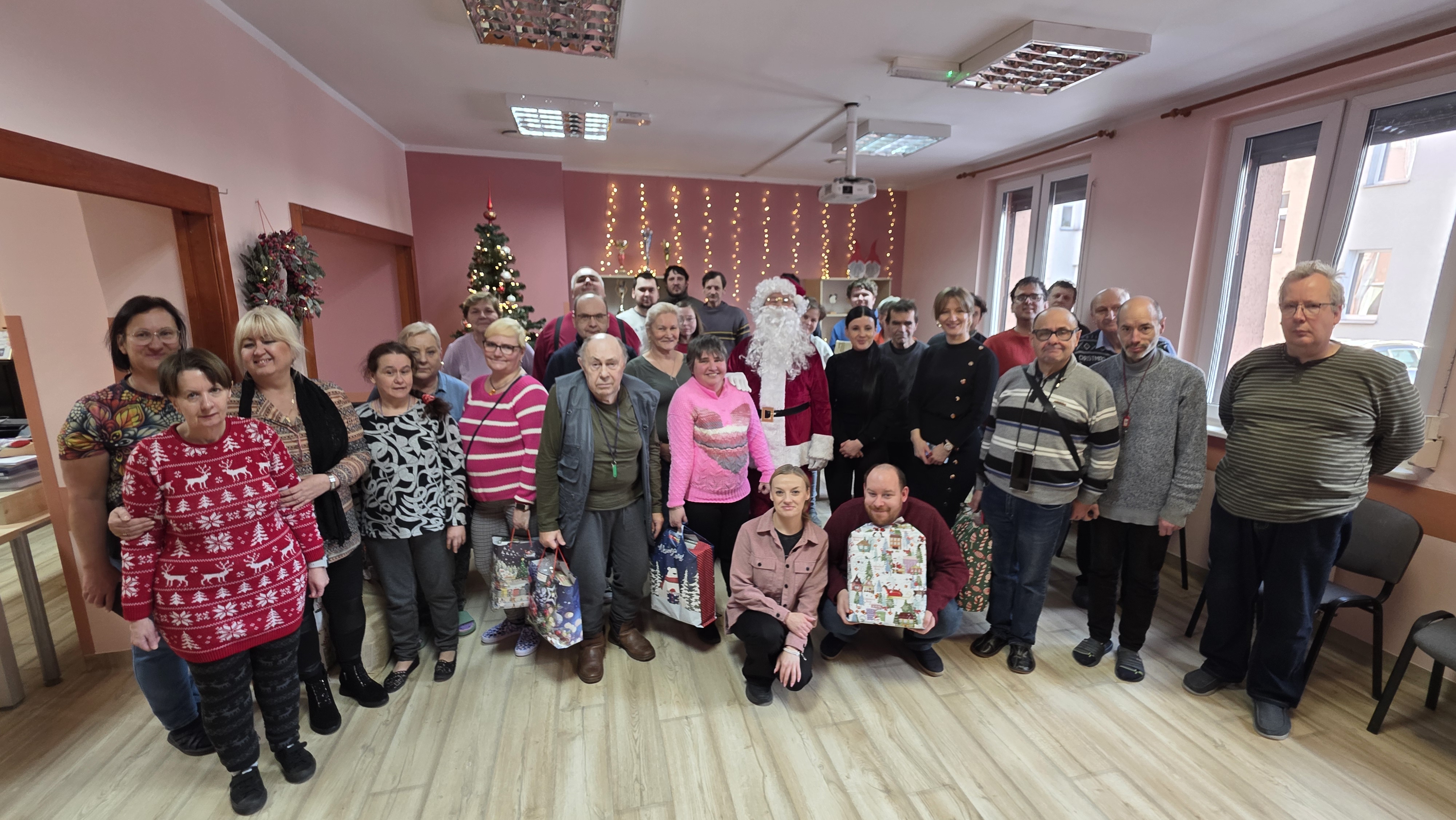 Grupa osób z paczkami pozuje do zdjęcia z Mikołajem.