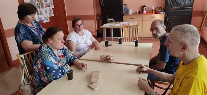Kobiety i mężczyźni siedzą przy stole ,na stole wieża z klocków.