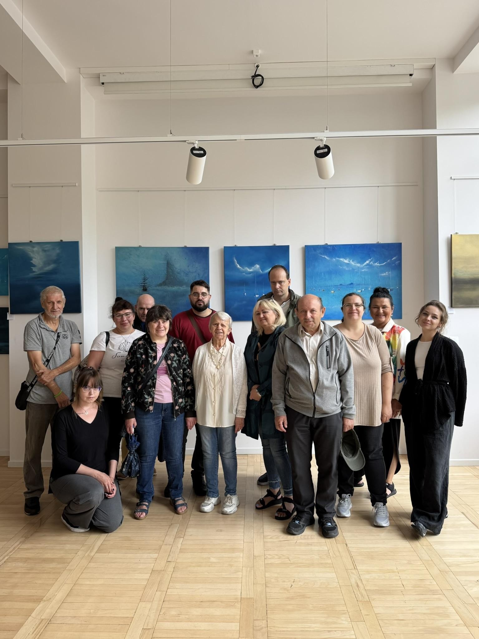 Grupa osób pozująca do zdjęcia. W tle widać ekspozycje obrazów.