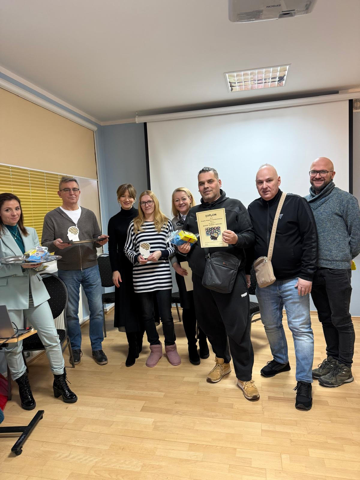 Grupa osób stojąca na tle białego ekranu, błękitnej ściany.