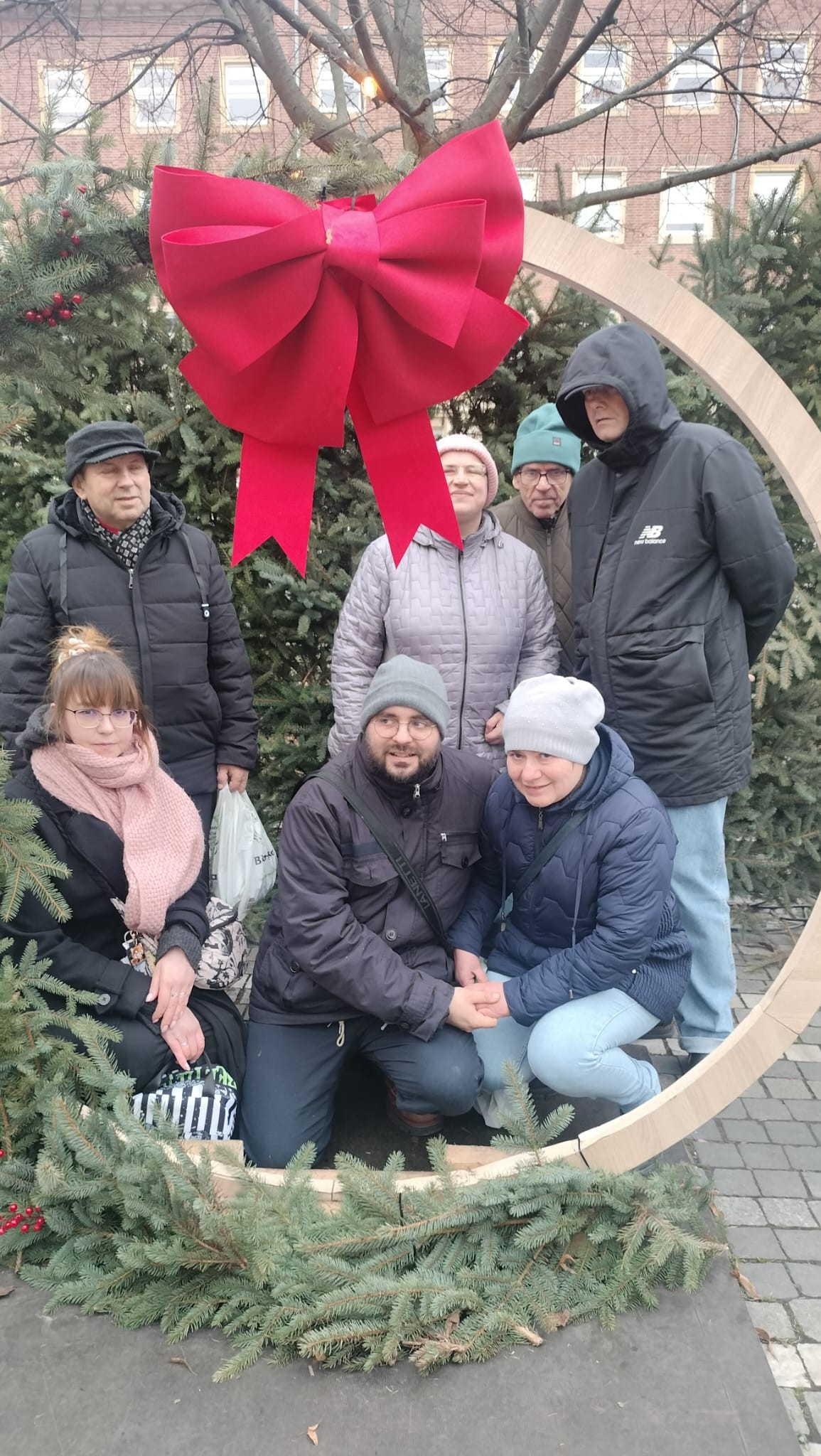 Grupa osób pozująca ze świąteczną dekoracją ze świerku.