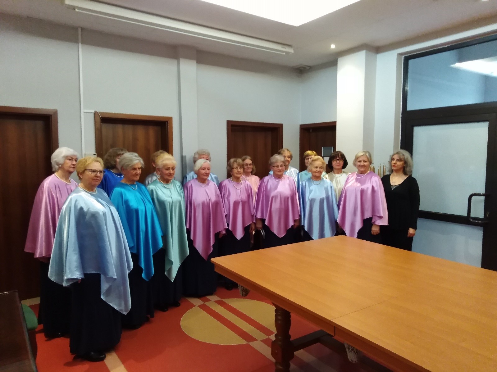 Grupa kobiet w kolorowych strojach prezentująca utwory muzyczne ustawiona w szyku chóralnym. 