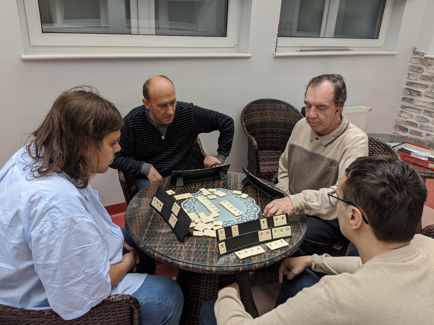 Czterech mężczyzn siedzących przy stole i grających w Rummikub 