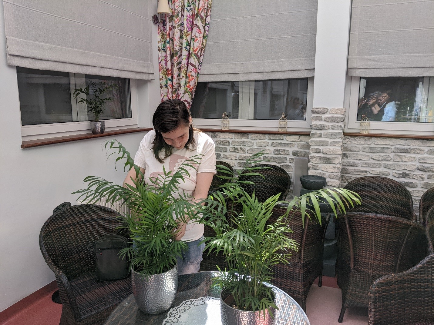 Kobieta o ciemnych włosach pielęgnująca rośliny doniczkowe.