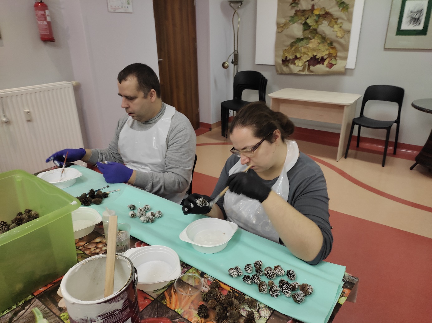 Mężczyzna i kobieta malują farbką szyszki. 