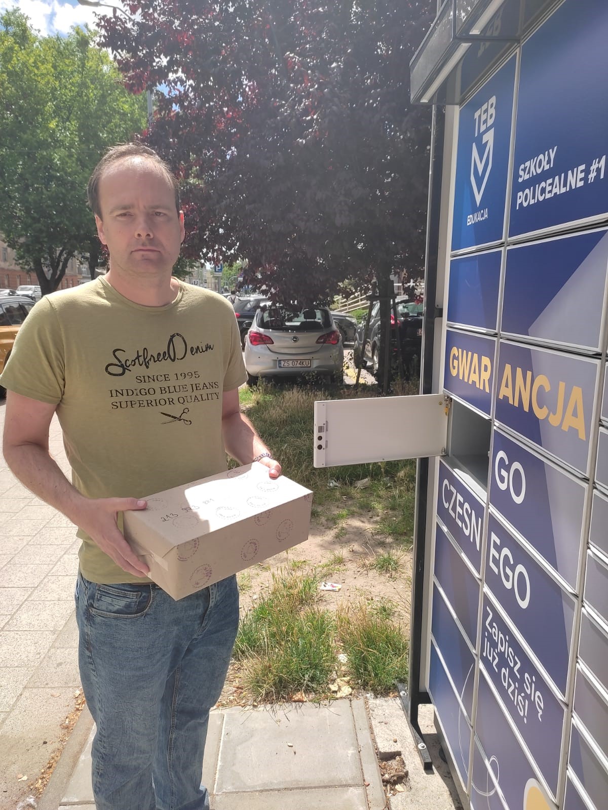Mężczyzna trzymający paczkę do nadania przy paczkomacie. 
