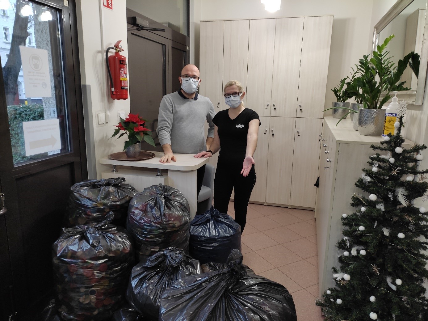 Kobieta i mężczyzna pozują przy, zebranych na cel dobroczynny, workach nakrętek.