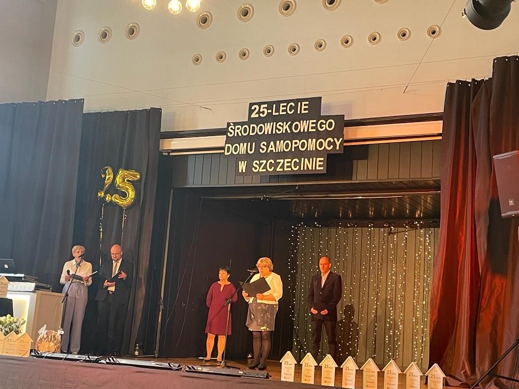 Grupa osób stojąca na scenie podczas recytowania wierszy. 