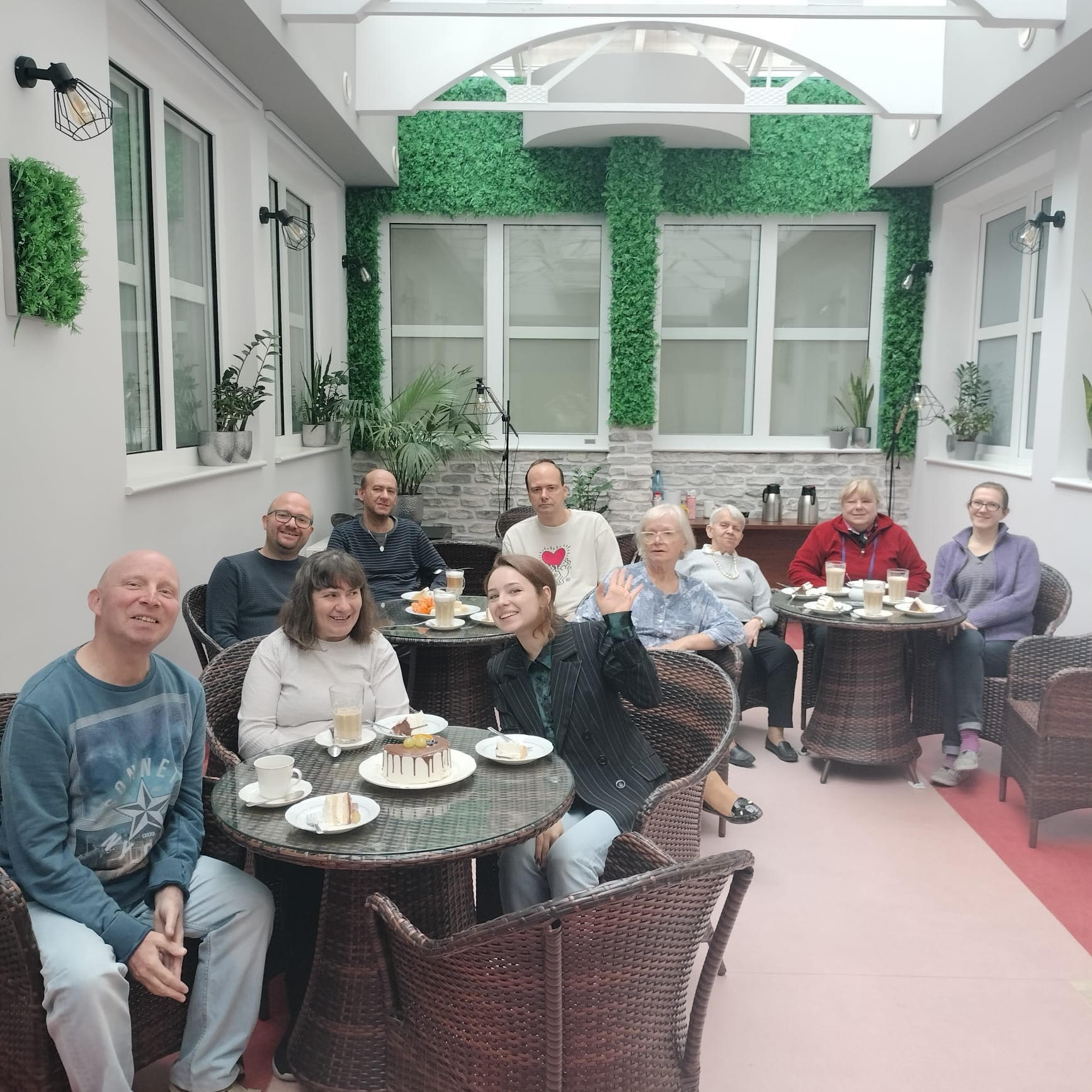 Grupa ludzi przy stolikach z kawą i tortem. 