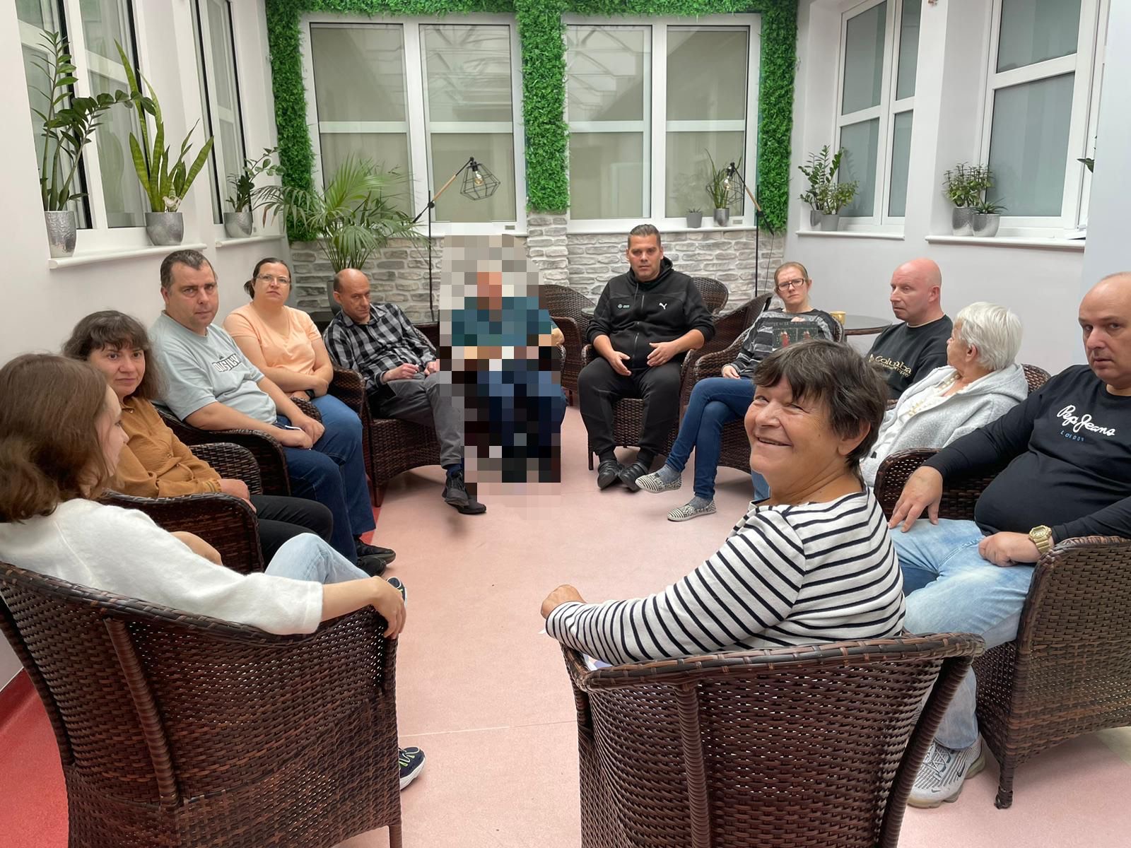 Grupa osób siedzie na fotelach w sali do zajęć terapeutycznych.