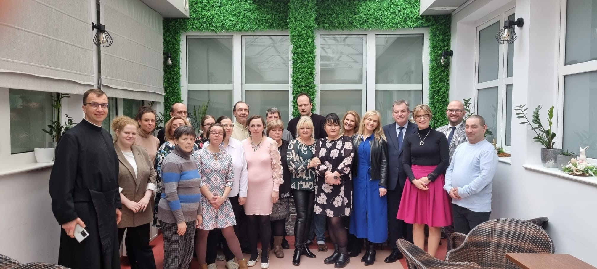 Grupa kobiet i mężczyzn na tle okien i ściany zieleni. 