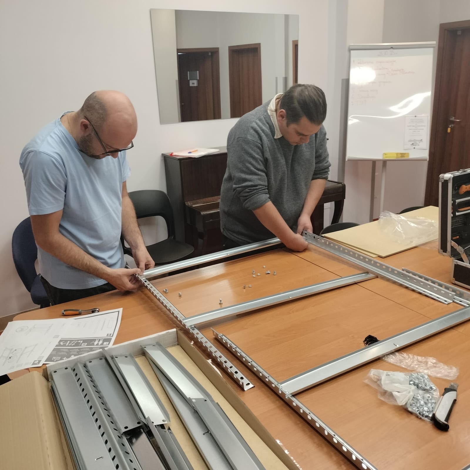 Dwóch mężczyzn skręcających metalowy regał. 